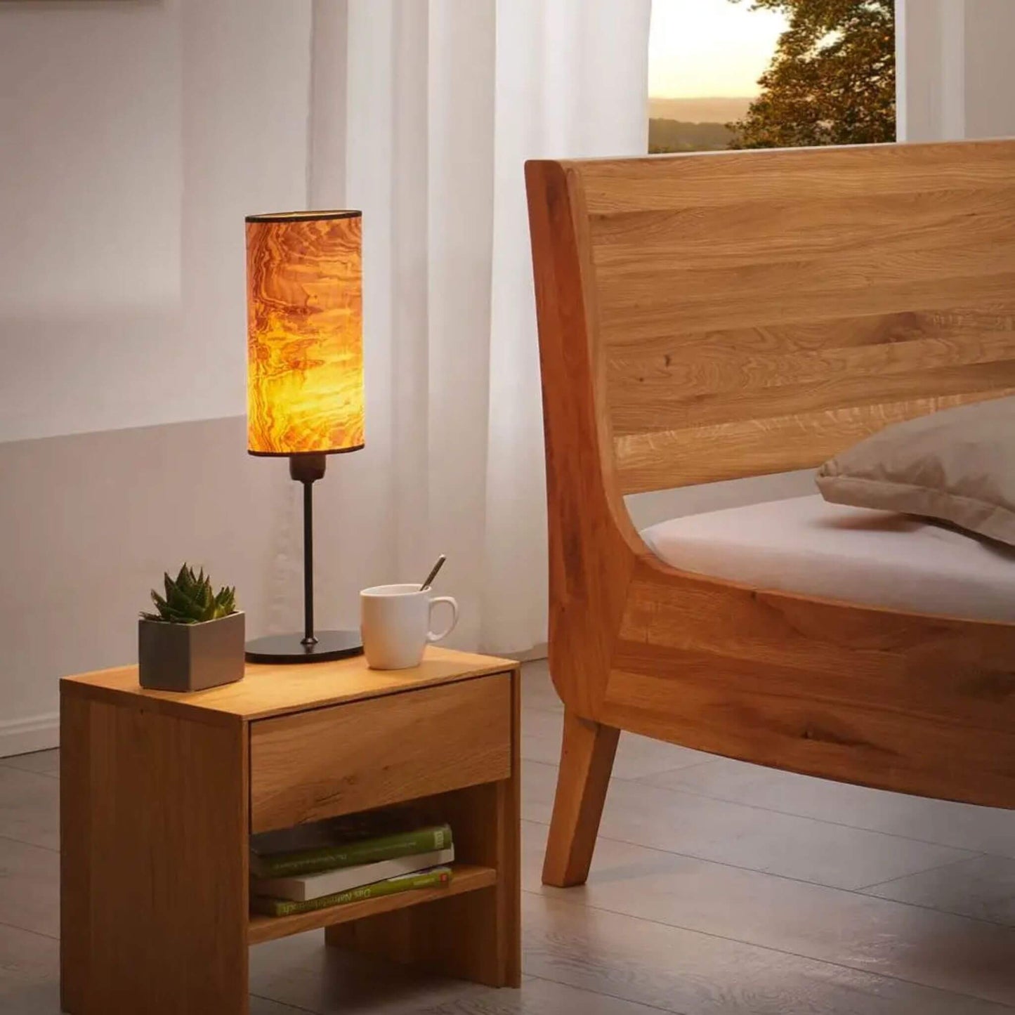 Nachttischlampe mit Holzfurnier-Schirm leuchtet warm auf einem Holznachttisch neben einem Bett.