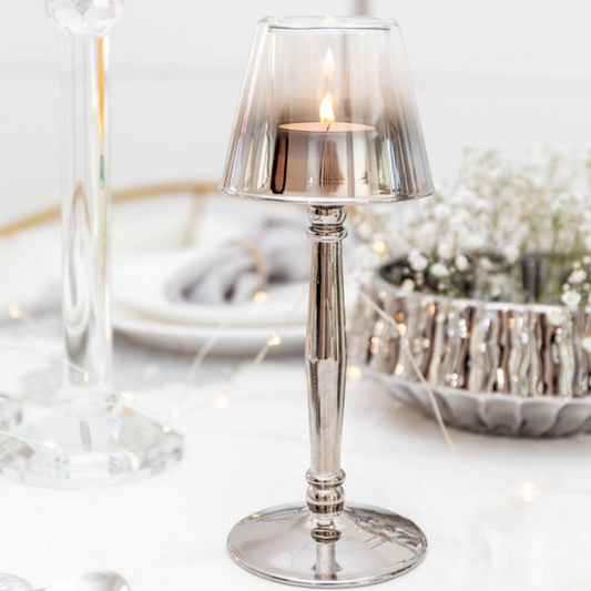 Aulica Kerzenhalter Silber mit brennendem Teelicht, warmes Licht durch Rauchglas-Schirm, weißer Tischhintergrund mit Dekoration
