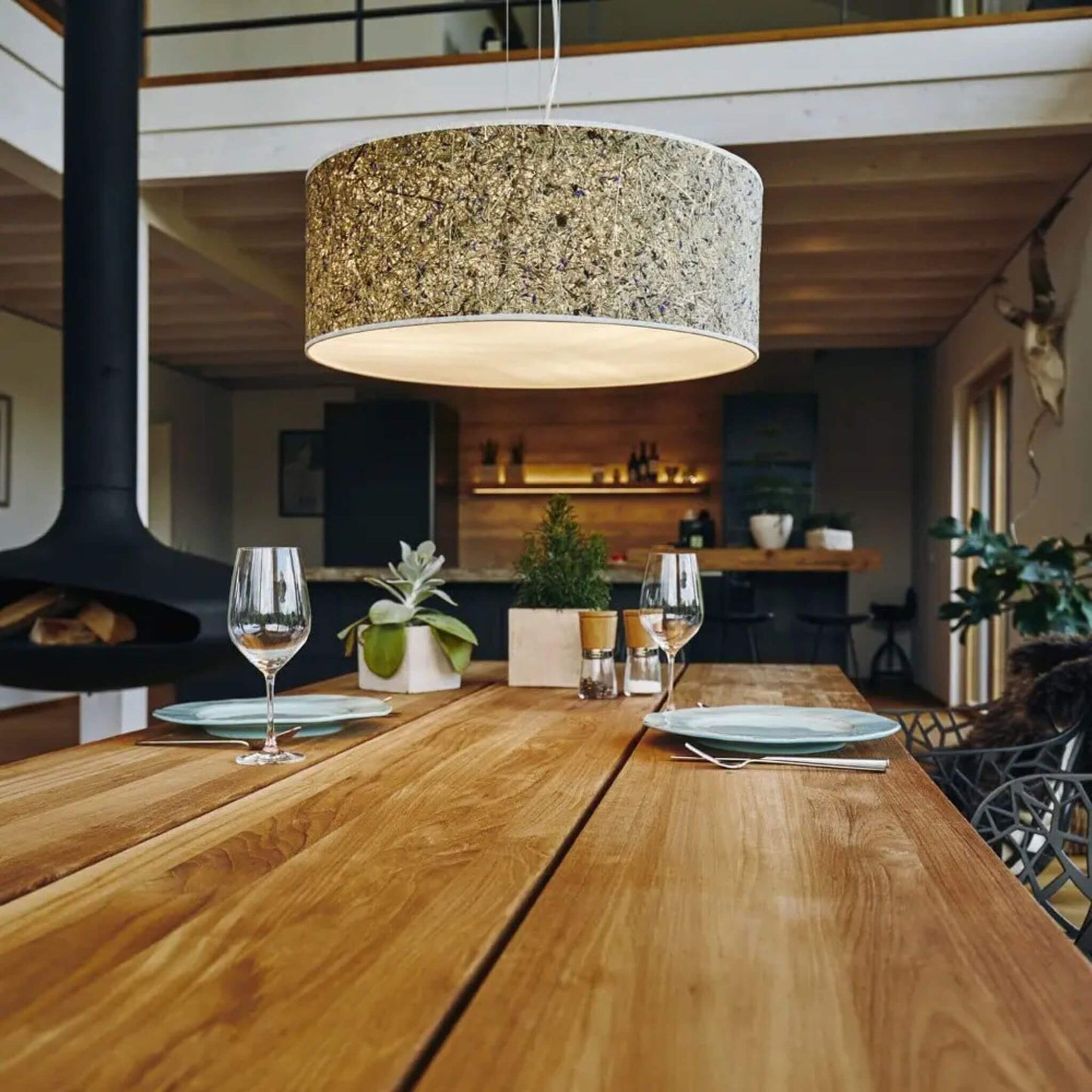 Pendelleuchte Discus 55 mit naturbelassenem Lampenschirm aus Almheu und Kornblumen, leuchtend über einem Esstisch aus Holz.