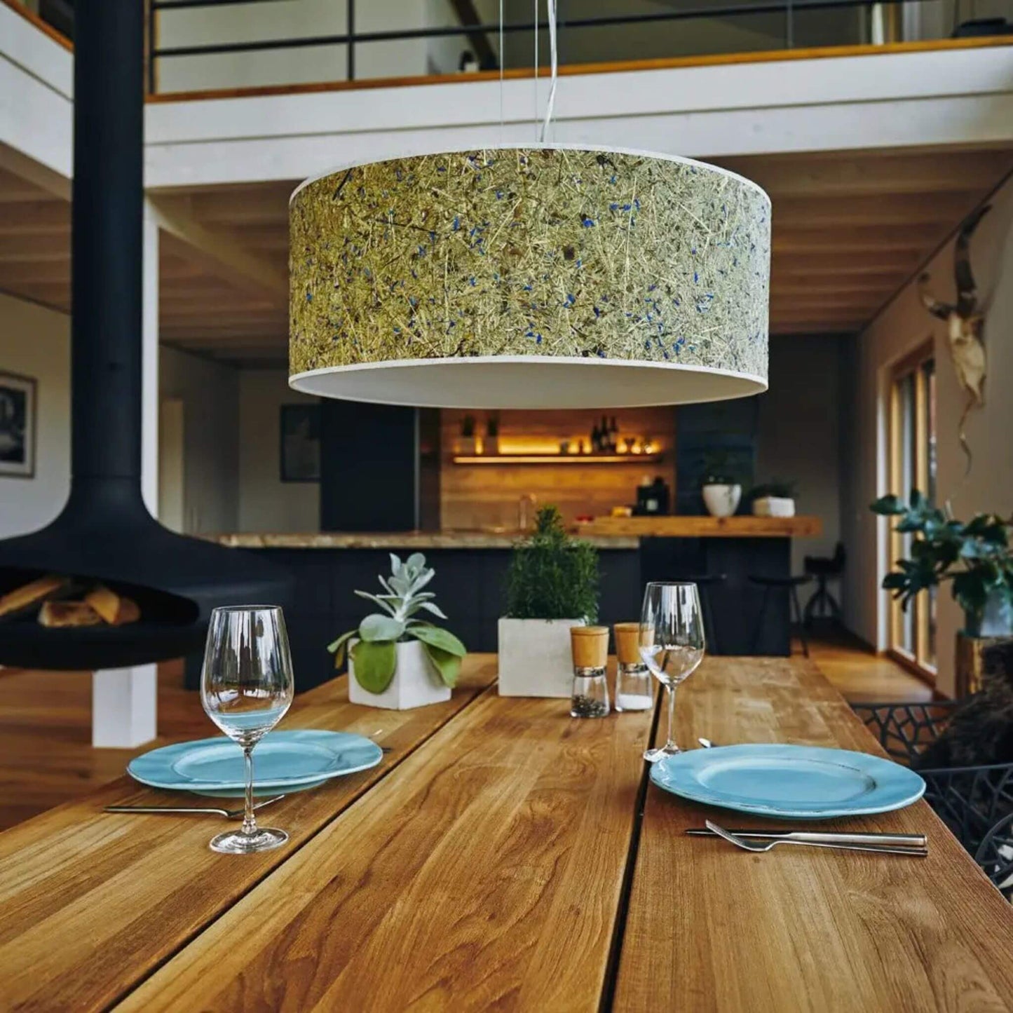 Discus 55 Pendelleuchte mit Lampenschirm aus Almheu und blauen Kornblumen über einem gedeckten Holztisch im Essbereich.