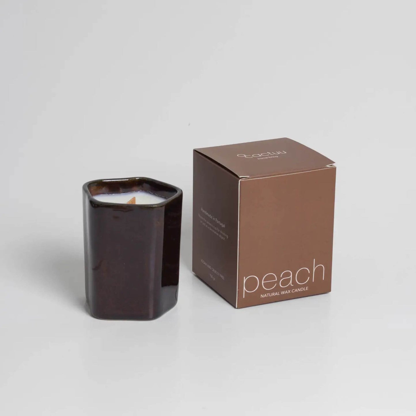 Dunkelbrauner Becher mit weißer Kerze, daneben eine braune Schachtel.
