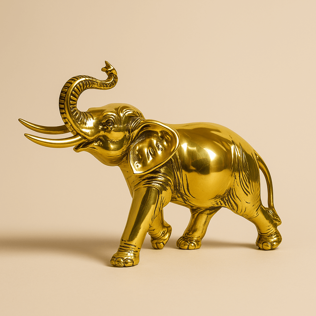 Glänzende goldene Elefantenfigur mit erhobenem Rüssel auf beigefarbenem Hintergrund.