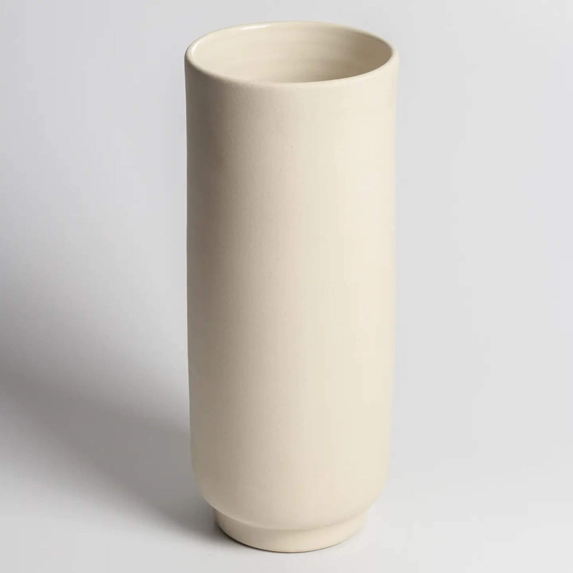 Hohe, zylindrische Vase aus hellem Steingut auf hellem Hintergrund.
