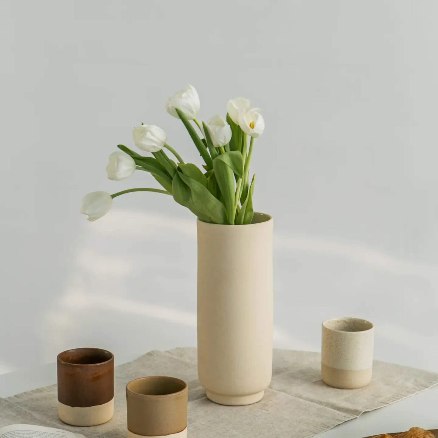 Hohe Steingutvase mit weißen Tulpen, daneben mehrere kleine Becher.