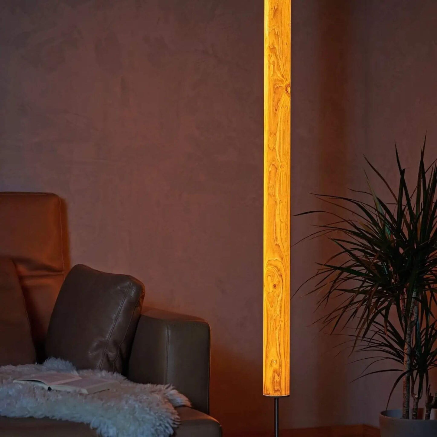 Leuchtende Stehlampe aus Eichenholz mit natürlicher Maserung, neben einem Ledersofa und einer Pflanze im Wohnzimmer.
