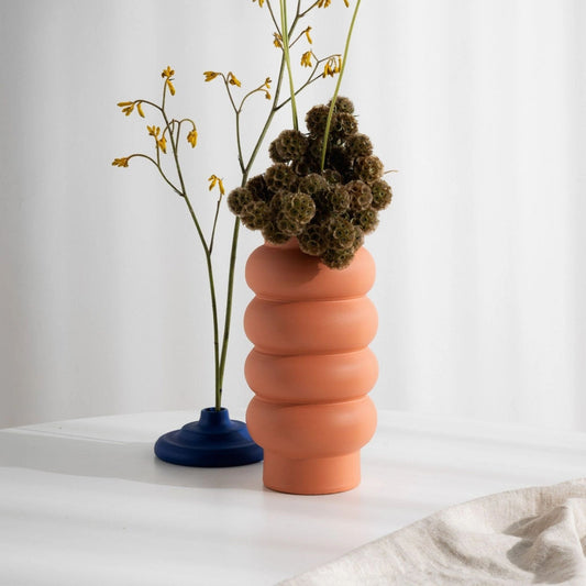 Korallenfarbene Vase in geschwungener Form mit Trockenblumen.