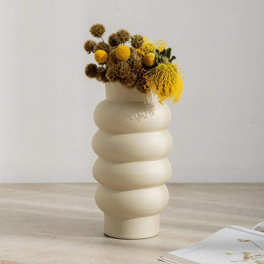 Hohe, off-white Vase mit geschwungener Spiralform, befüllt mit gelben Blüten.