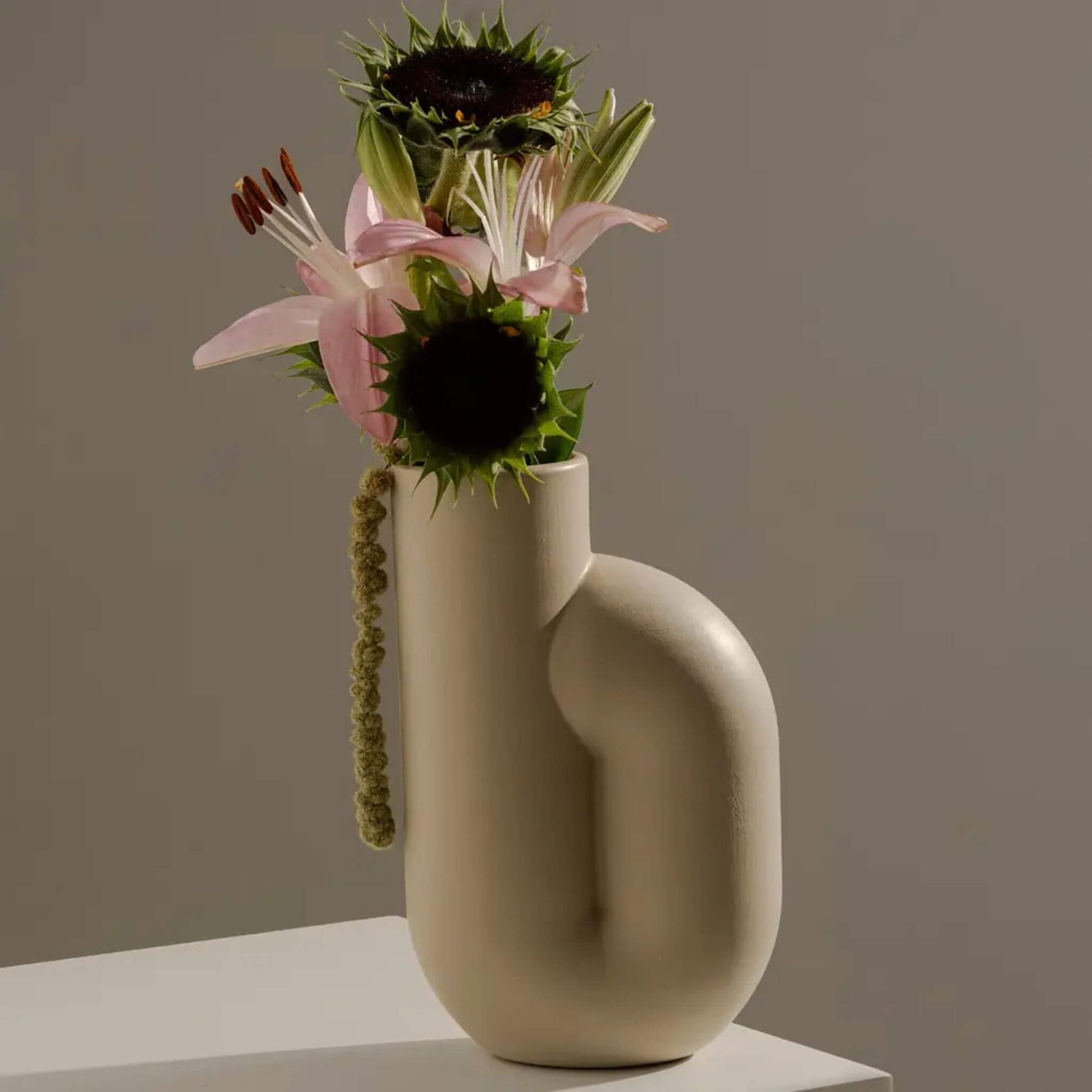Cremefarbene Vase mit Blumenarrangement aus Sonnenblumen und Lilien auf Tisch.