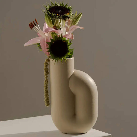 Cremefarbene Vase mit Blumenarrangement aus Sonnenblumen und Lilien auf Tisch.