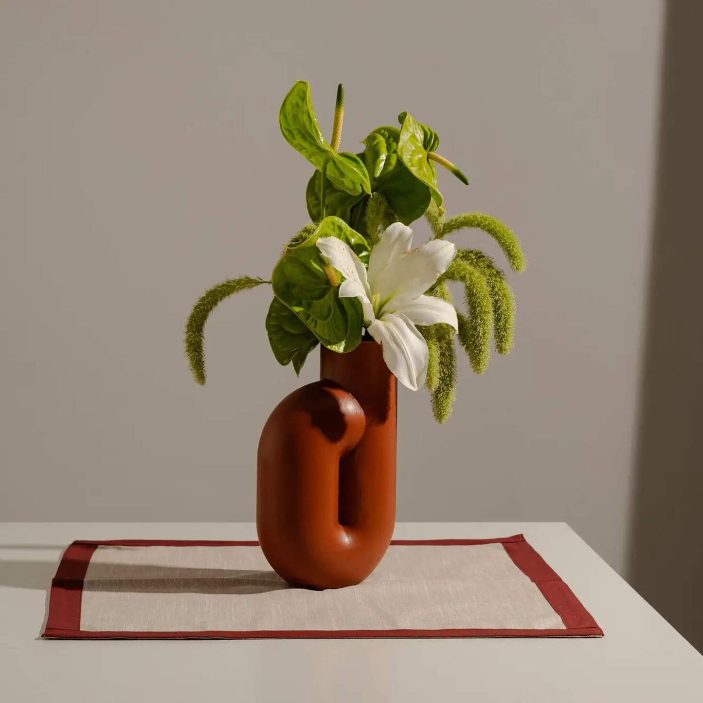 Terrakotta Vase mit Blumen auf hellem Podest, vor neutralem Hintergrund.