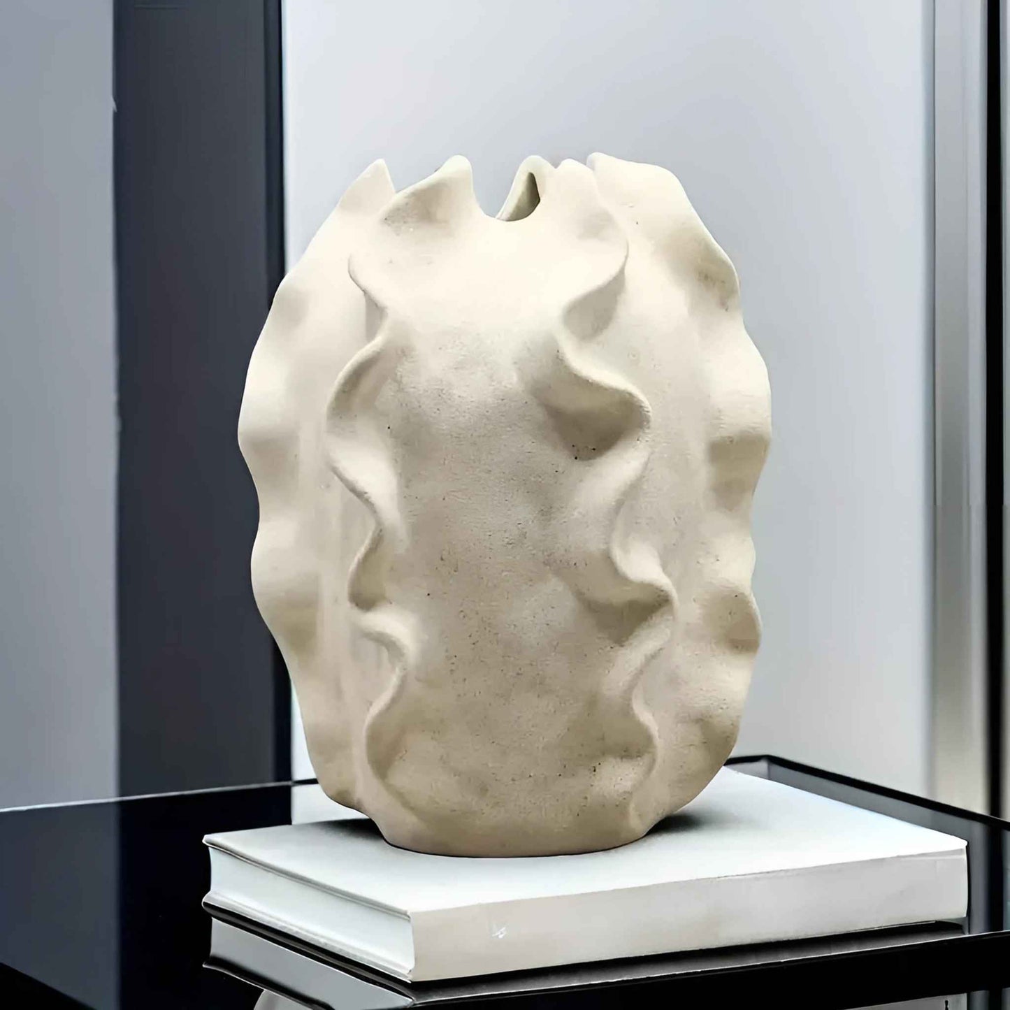 Beige Keramikvase im Boho-Chic-Stil mit organischen Wellenformen, dekorativ auf einem geschlossenen Buch auf einem Glastisch platziert.
