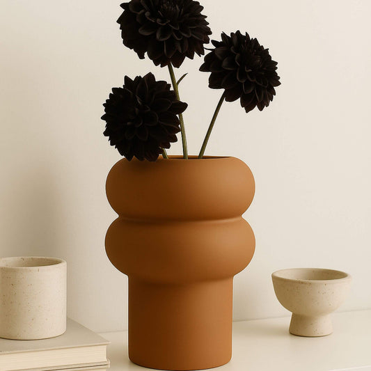 Hellbraune Vase mit runder Wellenform, darin drei dunkle Blütenstiele.