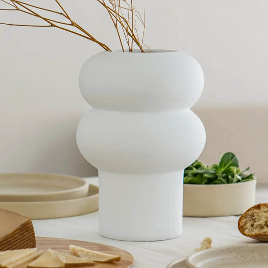 Weiße Vase mit runder Wellenform, befüllt mit dünnen braunen Zweigen.