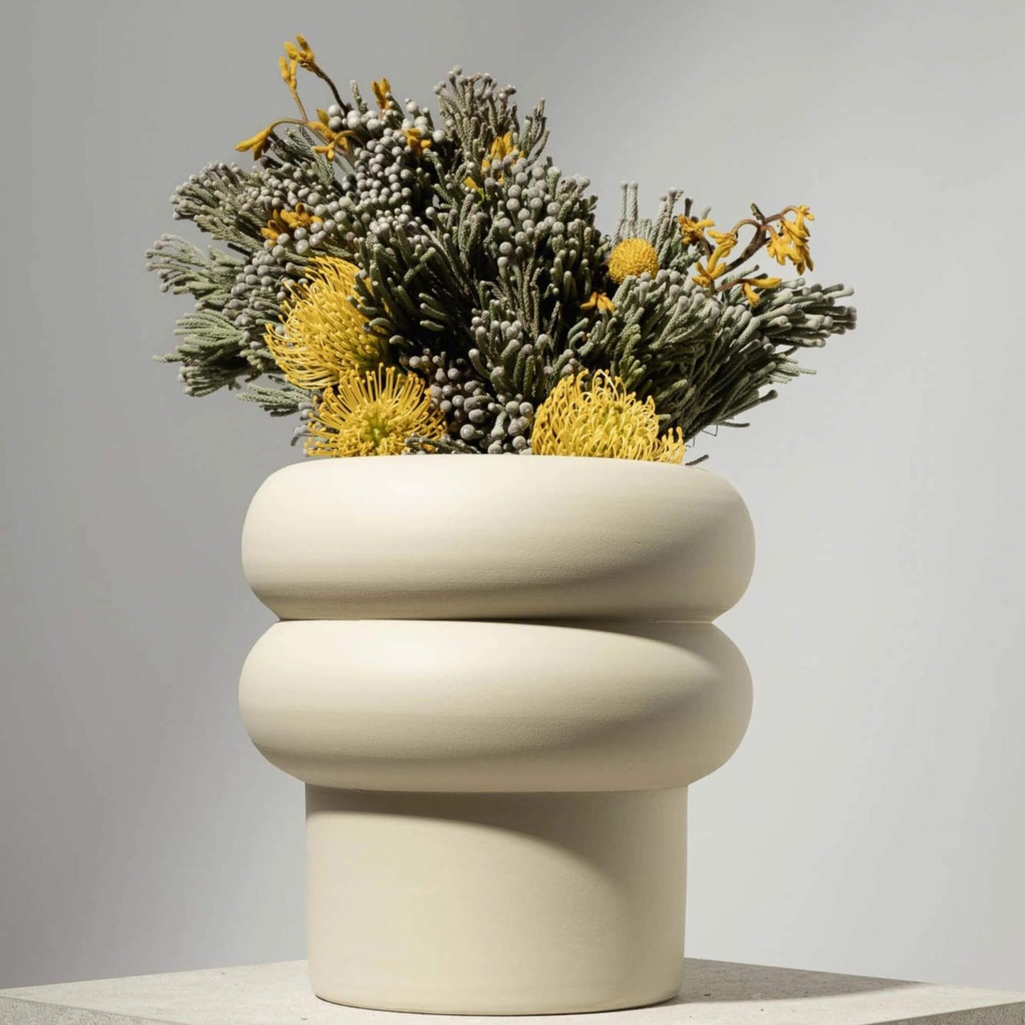 Großer, off-white Blumentopf mit runder Wellenform und gelb-grüner Bepflanzung.