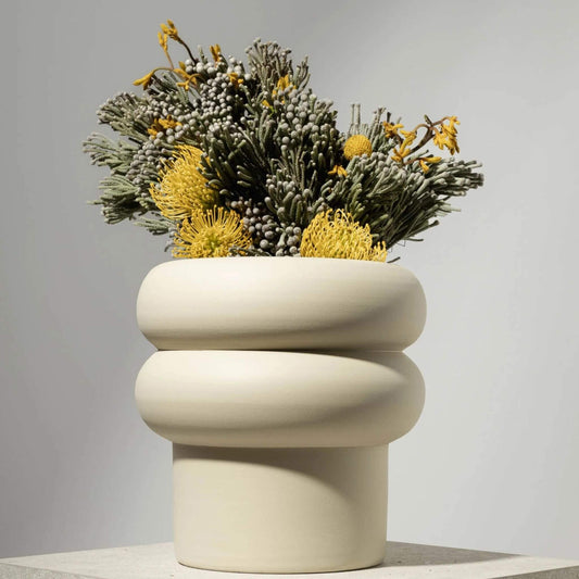 Großer, off-white Blumentopf mit runder Wellenform und gelb-grüner Bepflanzung.