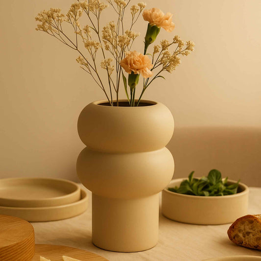 Off-White Vase mit runder Wellenform, befüllt mit grünen Zweigen und gelben Blüten.