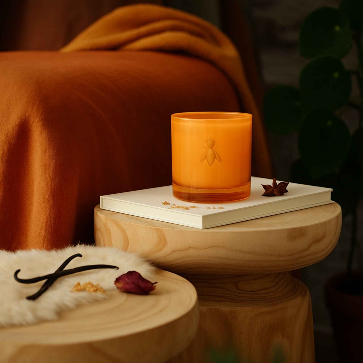 Handgemachte Duftkerze im orangefarbenen Glas mit Bienen-Relief, auf Buch im Wohnzimmer.