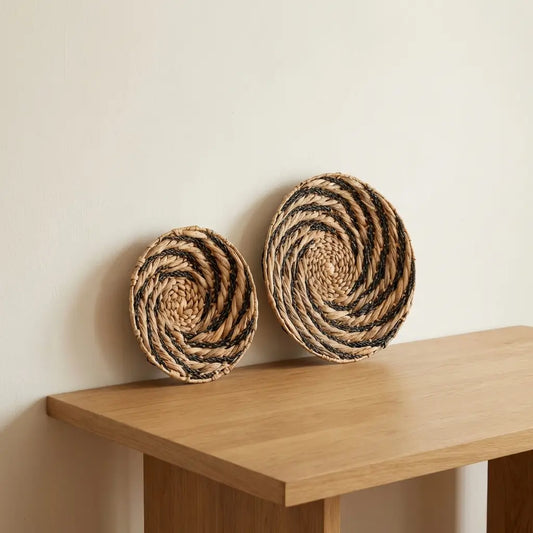 Handgefertigtes rundes Wanddekor Bandung aus nachhaltiger Wasserhyazinthe mit grafischem Muster in Schwarz und Natur auf einer Holzkonsole