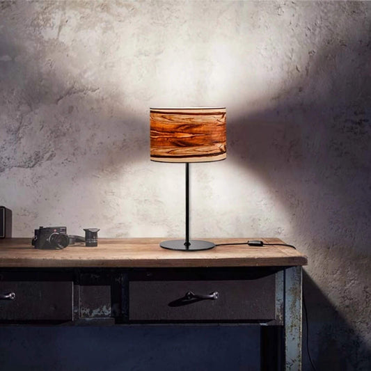 Arboreus 2 Tischlampe mit rundem Nussbaum-Satin-Lampenschirm, leuchtend auf einem rustikalen Schreibtisch mit Kamera und Zubehör.