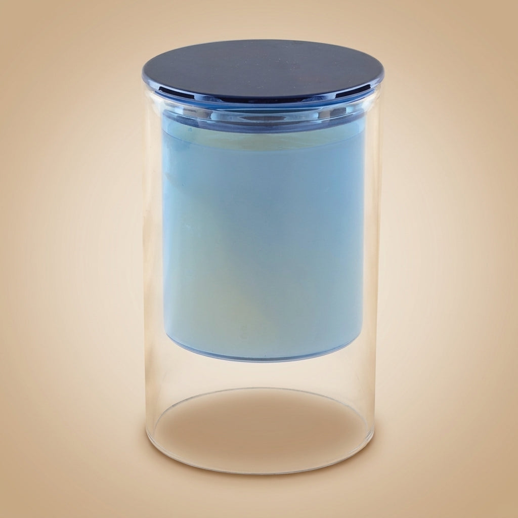 Aulica Duftkerze Zedernholz in klarem Glaszylinder mit blauem Wachseinsatz und blauem Metalldeckel, auf neutralem beigen Hintergrund