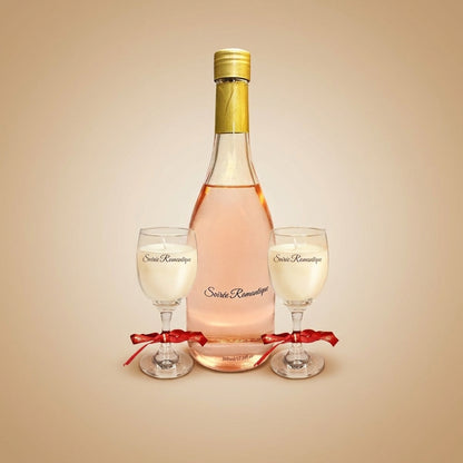 Aulica Soirée Romantique Set: Raumdiffusor in Weinflaschenform mit rosé-farbener Flüssigkeit und zwei Duftkerzen in Weinglas-Form, mit rotem Band zusammengebunden, auf beigem Hintergrund