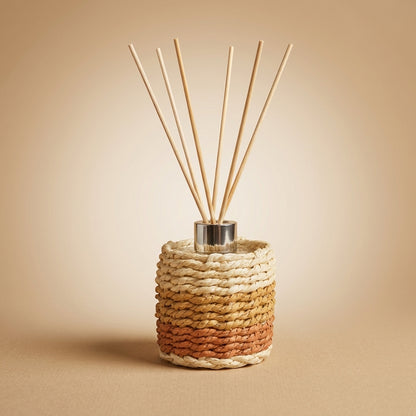 Aulica Raumdiffusor Moschus, geflochtener Mantel in Creme-Terrakotta-Verlauf mit silbernem Metallverschluss und Reedstäbchen, auf neutralem beigen Hintergrund