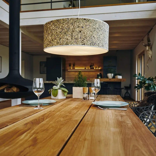 Pendelleuchte Discus 55 mit naturbelassenem Lampenschirm aus Almheu und Kornblumen, leuchtend über einem Esstisch aus Holz.