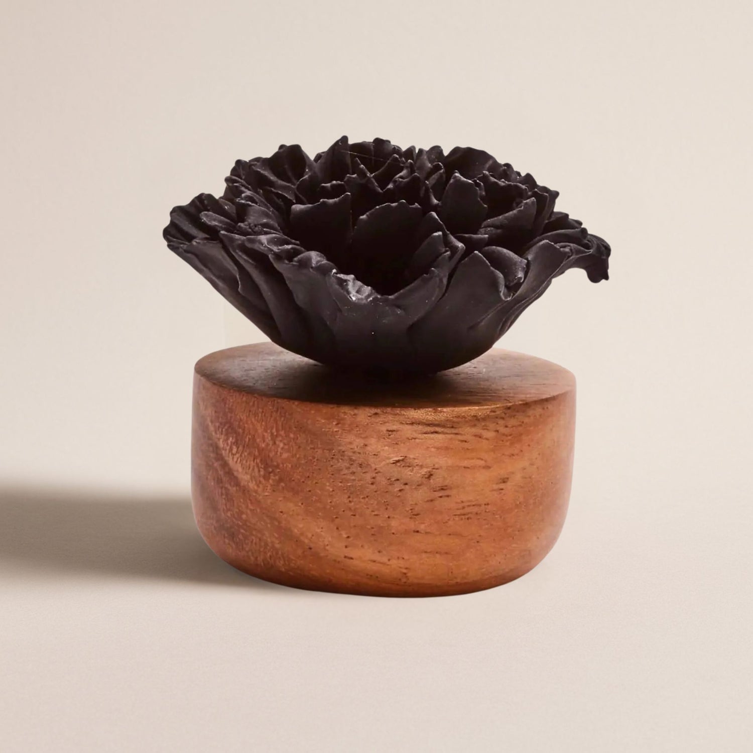 Nahaufnahme des schwarzen Blütendiffusors auf rundem Holzsockel vor weißem Hintergrund.