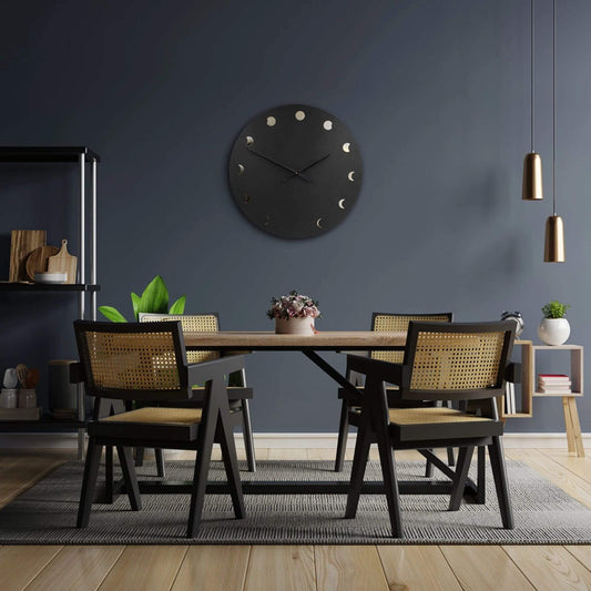 Moderne schwarze Wanduhr mit Mondphasen-Design über einem Esstisch in elegantem, dunklem Interieur.