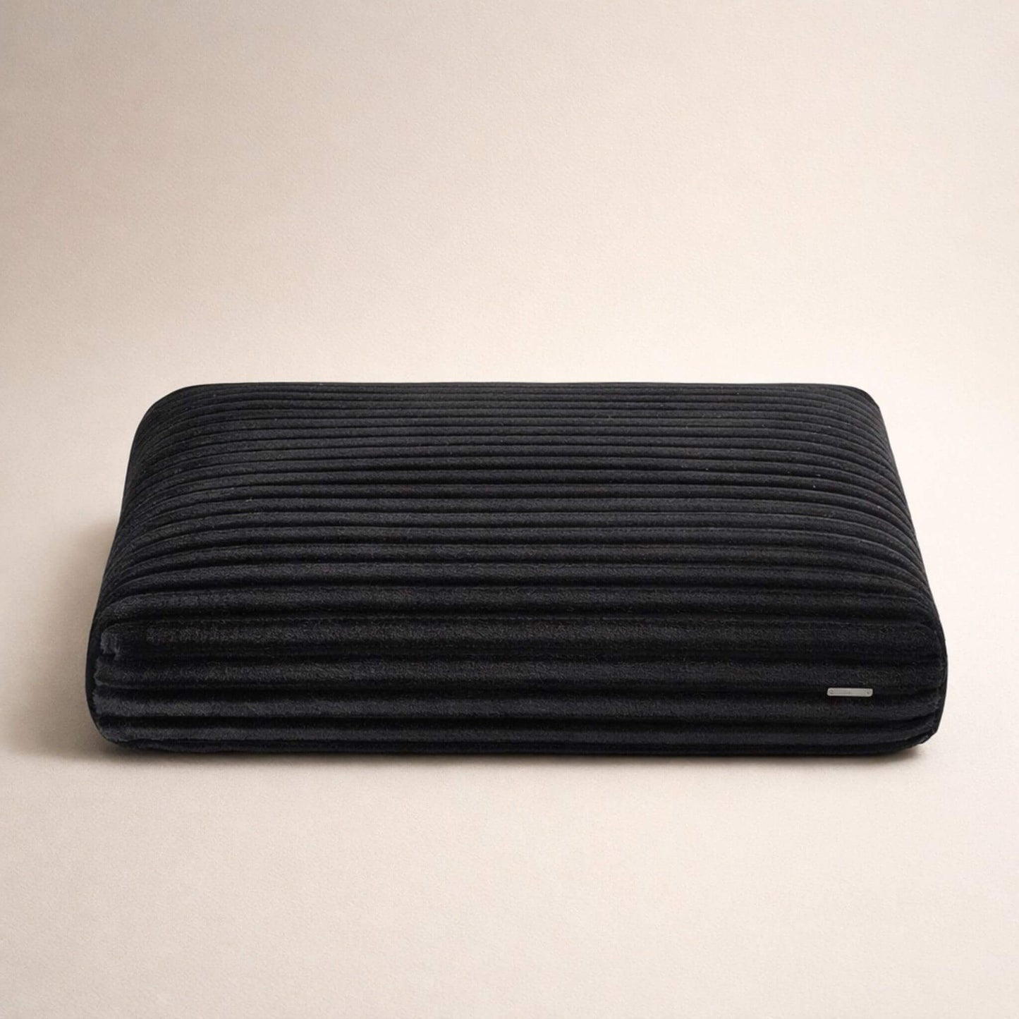 Rechteckiges schwarzes Hundekissen mit gerippter Stoffstruktur vor hellem, neutralem Hintergrund.