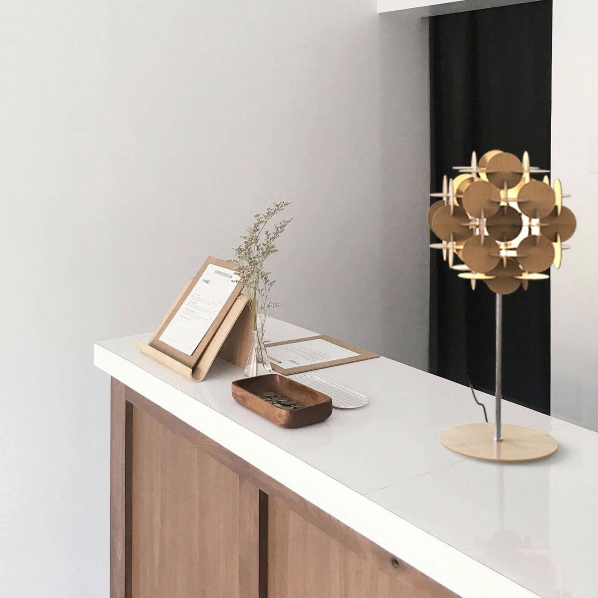 Tischlampe mit Holzplattenschirm auf einer weißen Theke in modernem Interieur mit minimalistischer Dekoration.