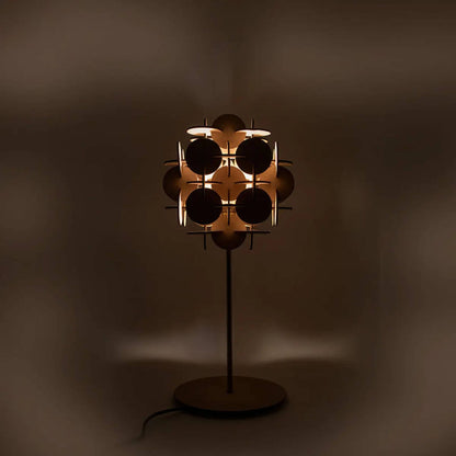 Die Tischlampe strahlt warmes Licht in einem dunklen Raum aus und betont die geometrische Struktur des Schirms.