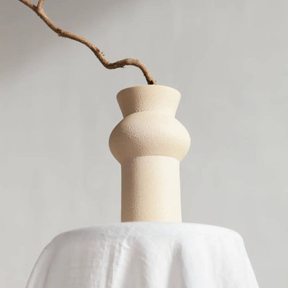 Cremefarbene Vase mit bauchiger Mitte, darin ein einzelner Ast mit dünnem Zweig.