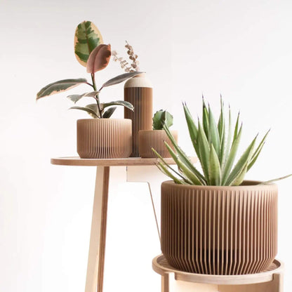 Innenraumszene mit PRAHA Pflanzkübel groß, aus Holz mit feiner Rillenstruktur, und anderen Gefäßen im Hintergrund.