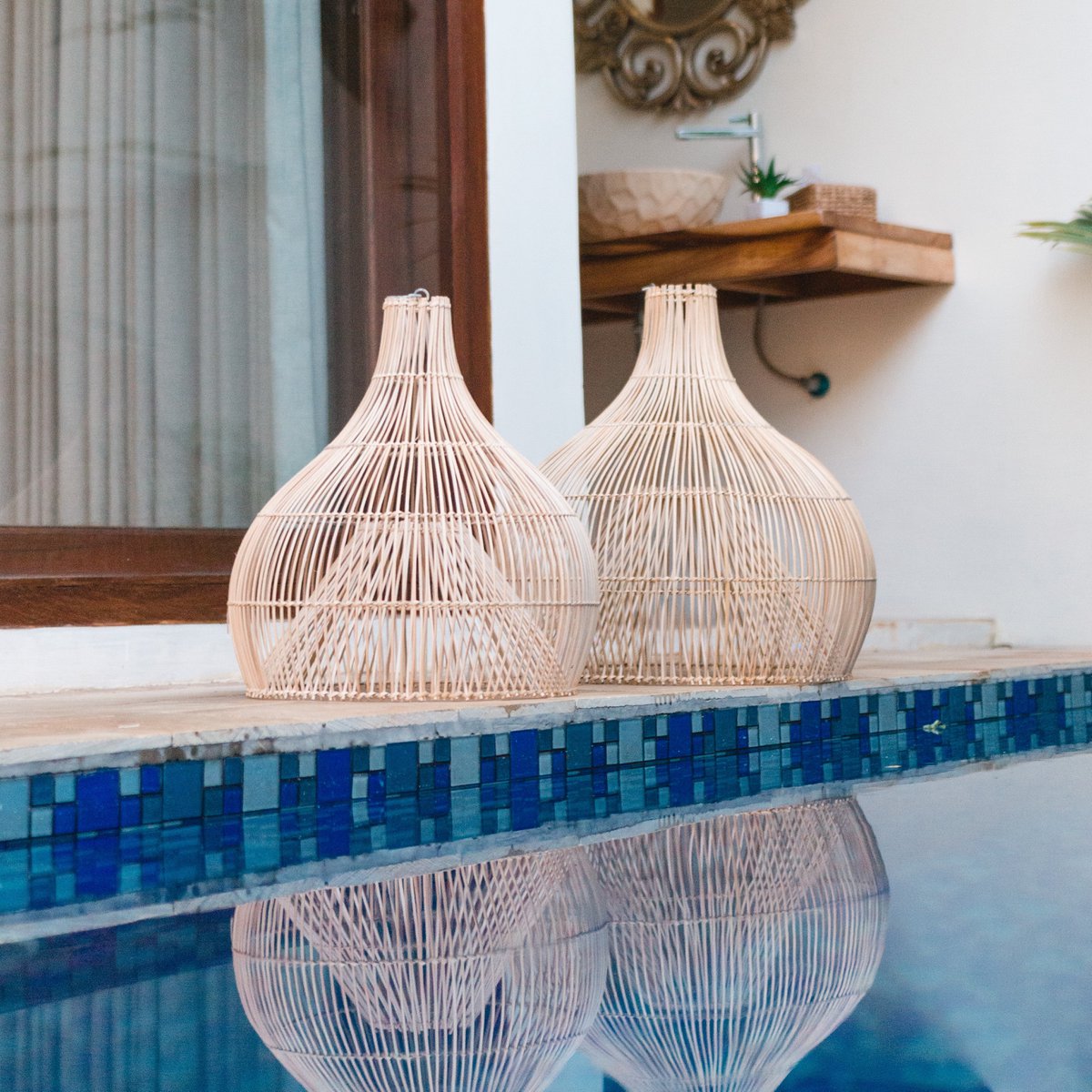 Rattan-Lampenschirme Alam am Poolrand platziert, natürliche Flechtstruktur mit Spiegelung im Wasser.