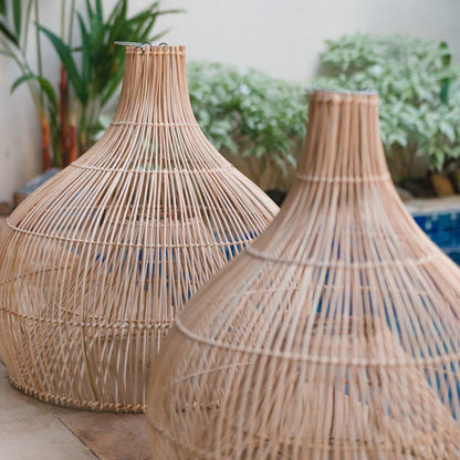 Zwei handgeflochtene Rattan-Lampenschirme Alam im Außenbereich mit Pflanzen im Hintergrund.