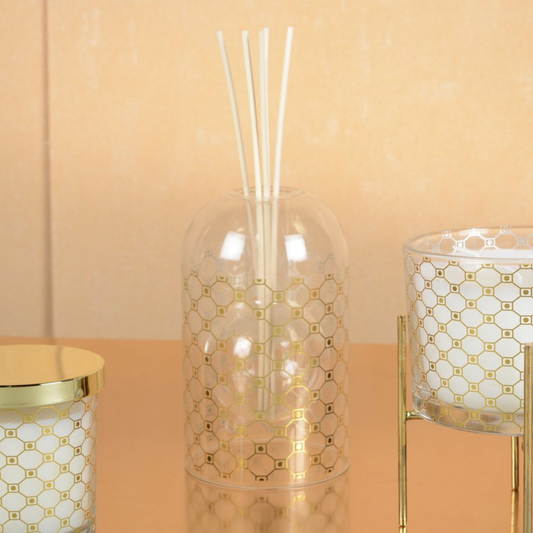 Aulica Raumdiffusor Gold Wabenmuster flankiert von zwei passenden Aulica-Kerzen im selben Design auf reflektierender Oberfläche