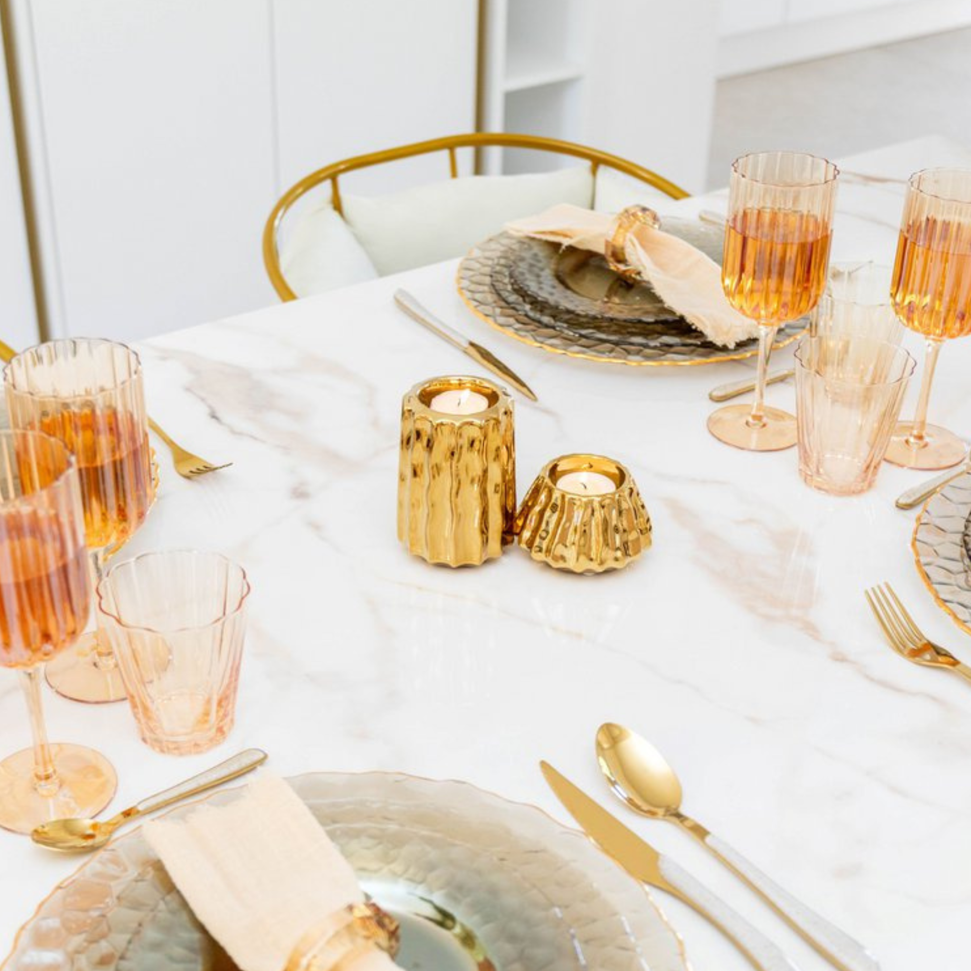 Aulica Teelichthalter Gold auf gedecktem Marmortisch mit rosé Gläsern und Goldbesteck, seitliche Perspektive, weißes Interieur