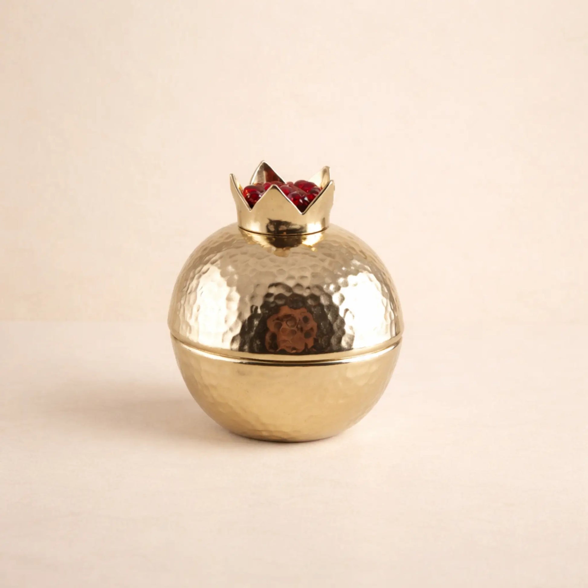 Goldene Granatapfel-Box aus Aluminium vor hellem beigen Hintergrund im minimalistischen, eleganten Stil