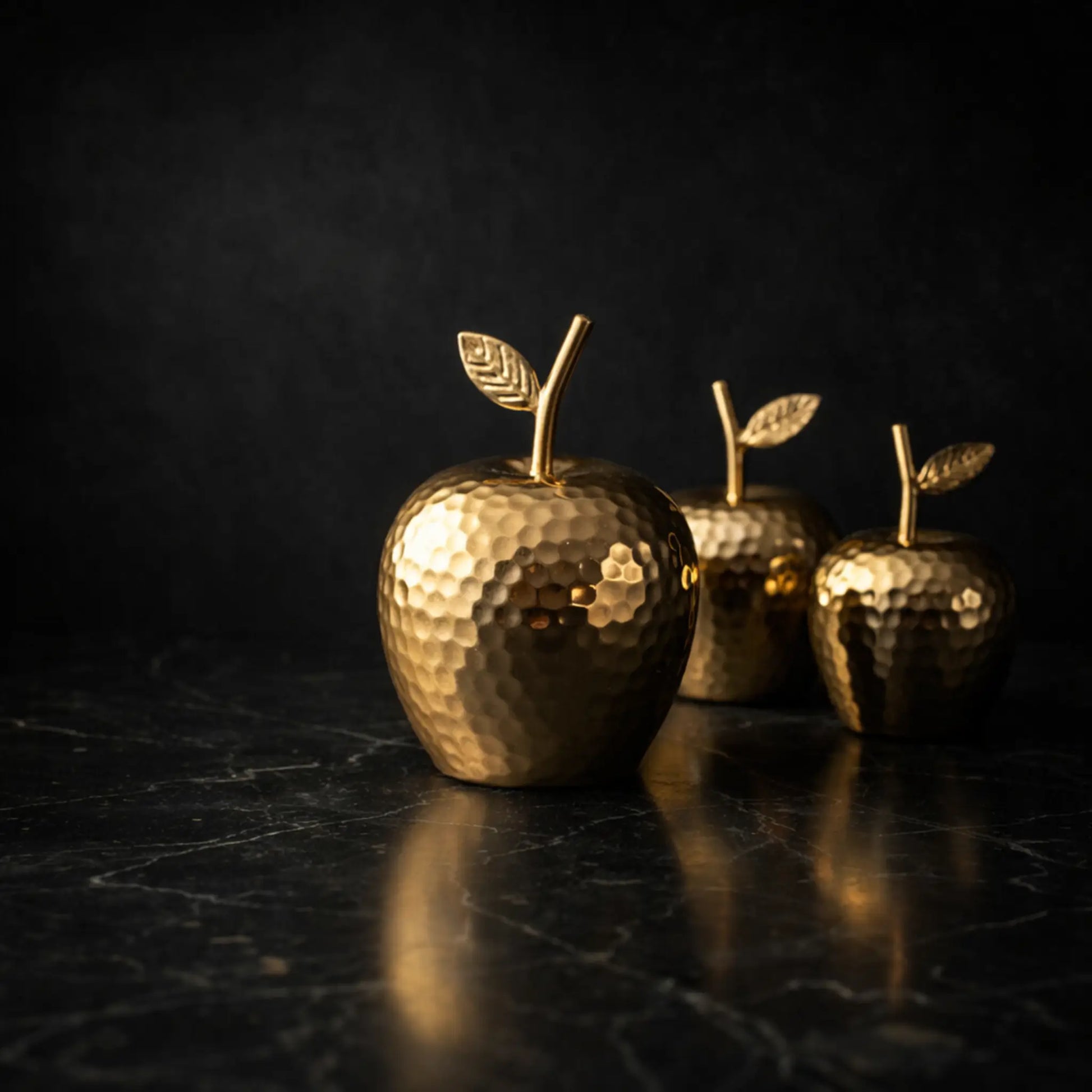 Goldene Deko-Äpfel auf schwarzem Marmortisch mit dunklem Hintergrund.