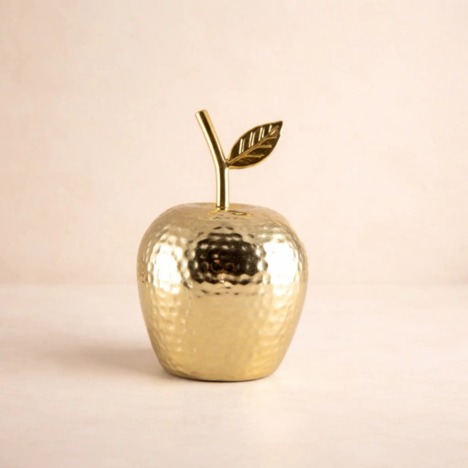 Goldener Deko-Apfel aus Aluminium vor beigem Hintergrund.